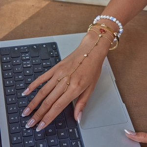 Gold hand harness with red heart pendant and layered bracelets on laptop keyboard
