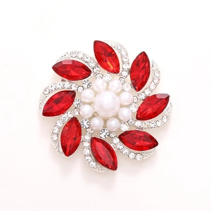 Elegante broche de flor plateado con cristales rojos y perla central en fondo blanco