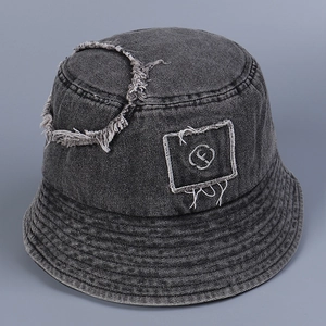 Close-up of distressed denim bucket hat featuring letter embroidery and frayed fringe edges