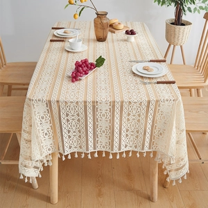 Elegant beige lace tablecloth with tassel edges on a wooden table for home dining