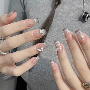 Detail of square nails with nude pink base, grey gradient, glitter and heart rhinestones