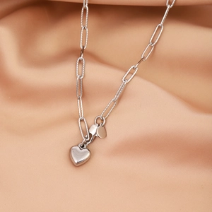 Detail of silver heart pendant on paperclip chain over elegant champagne satin fabric