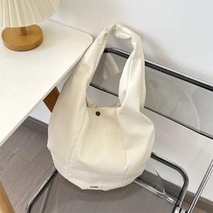 Detalle del bolso tote de pana crema con sutil textura de rayas y etiqueta de la marca