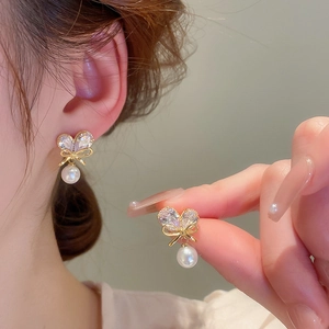 Elegant gold bow earrings with cubic zirconia and round pearls shown on model's ear