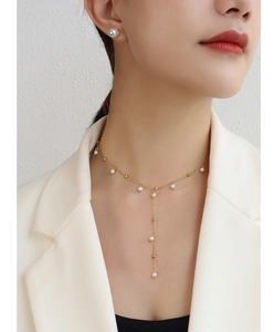 Detail of Y-shaped gold plated pearl necklace with drop tassel on a model in a white blazer