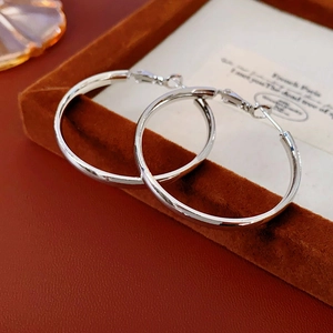 Close-up of minimalist silver hoop earrings on orange velvet tray with French card