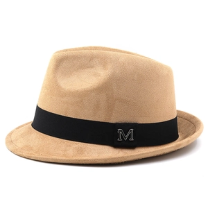 Close-up of the silver M logo on a camel suede fedora hat with black grosgrain ribbon