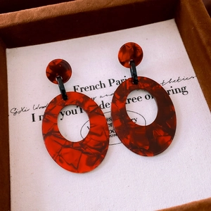 Macro shot of oval acrylic earrings with amber tortoise shell texture on white card