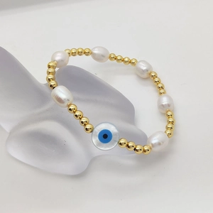 Baroque pearl bracelet with gold beads and blue evil eye charm on minimalist stand