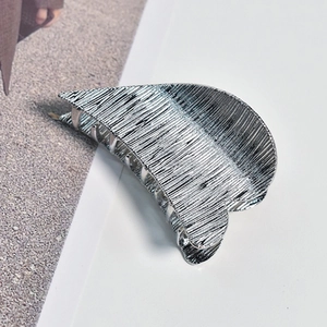 Close-up of a silver medium metal hair claw with brushed texture on a minimalist surface
