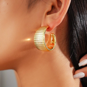 Close-up of model wearing a chunky gold C-shaped earring with elegant spiral thread texture