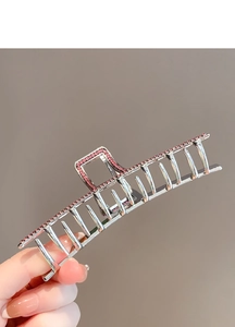 Detail of silver metal shark hair claw clip with pink rhinestones shown in hand