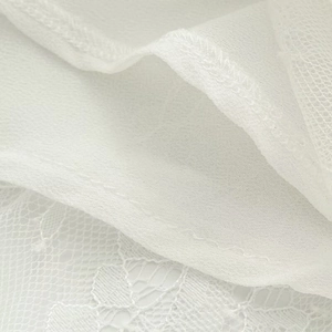 Dettaglio ravvicinato della trama in pizzo bianco e chiffon con cuciture di alta qualità