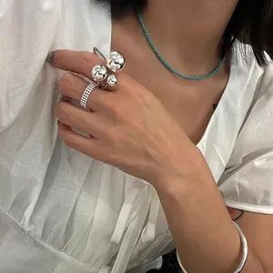 Close-up of minimalist turquoise bead necklace and silver multi-ball rings on a model