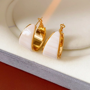Close-up of gold plated resin hoop earrings with white inlay on a premium display