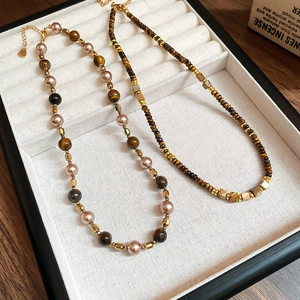 Detail of vintage tiger eye and pearl necklaces with gold lobster clasps in a jewelry box