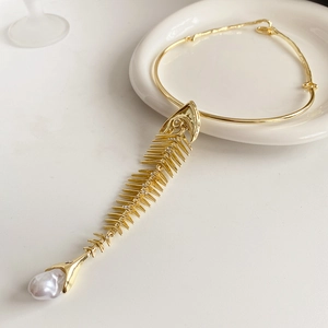 Macro shot of gold fishbone pendant necklace with baroque pearl on a white ceramic plate