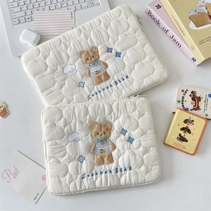 Detalle de la funda acolchada crema para portátil con bordado de oso y patrón de nubes