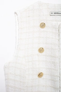 Detailed macro view of white tweed fabric texture and gold buttons on sleeveless vest