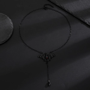 Detail shot of black gothic bat necklace with red eyes on a dark textured rock background