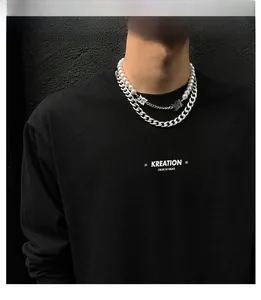 Détail d'un collier hip-hop superposé avec perles blanches, chaîne argentée et pendentif gothique