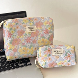 Quilted floral makeup bag set with zipper and embroidered label beside a laptop