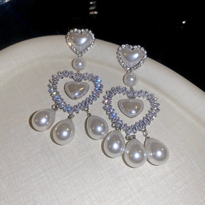 Dettaglio di orecchini a cuore in argento con cristalli scintillanti e perle a goccia