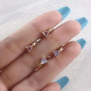 Vue macro de boucles d'oreilles huggies dorées avec zircons roses et violets en cœur