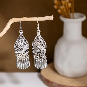 Detail view of bohemian hollow teardrop earrings with metal tassels on a wooden branch