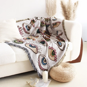 Detail of bohemian woven blanket with abstract eye patterns and fringe on a sofa