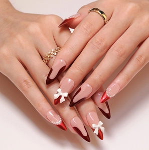 Detail of red French almond nails with 3D white bows and pearl embellishments