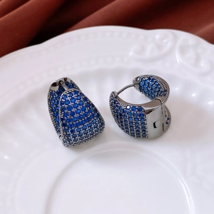 Detailed view of asymmetric grey metal hoop earrings with sparkling blue zircon inlays