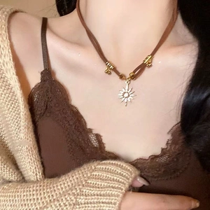 Close-up of golden sun pendant with white stone on brown cord necklace worn by model
