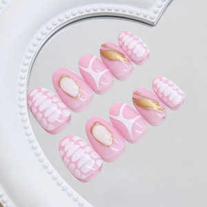 Pink press-on nails with golden strokes and white honeycomb grid pattern on a white tray
