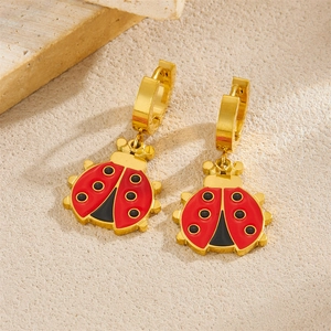 Cute ladybug earrings in red and gold finish on a textured beige stone background