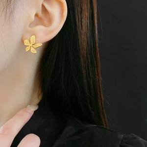Macro view of matte golden five-petal flower stud earring on a model with black background