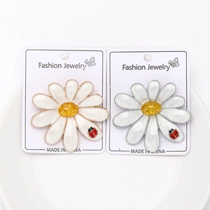 Detail view of two daisy brooches with enamel petals and ladybug accents on a card