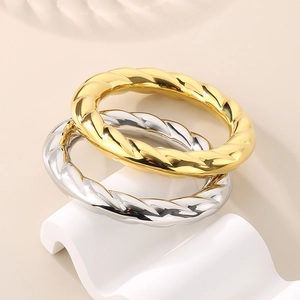 Polished hollow twisted spiral bangle in 18k gold and silver finish on a wave stand