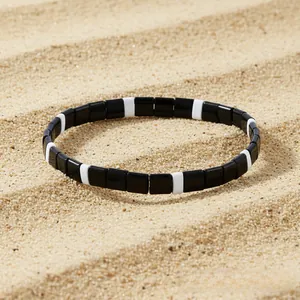 Detail of bohemian black and white Tila bead stretch bracelet on a sandy beach background