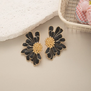 Detailed close-up of matte black daisy earrings with gold edges and textured center
