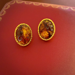 Close-up of vintage resin earrings with amber texture and gold engraved metal edges
