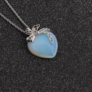 Close-up of translucent opal heart pendant with a silver bow clip on a textured dark base
