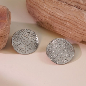 Detailed macro view of silver star-engraved round stud earrings on a natural stone base