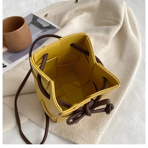 Top view of yellow hand-woven bucket bag with dark brown strap on beige fabric
