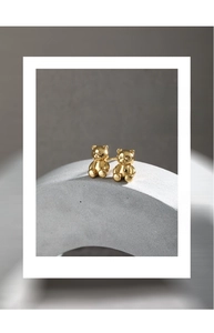 Detailed close-up of 18K gold teddy bear studs on a minimalist grey geometric stand