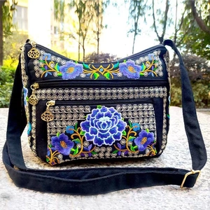 Close-up of vibrant floral embroidery on a black canvas crossbody bag with gold zippers