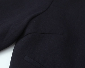 Close-up of premium twill fabric texture and stitching details on dark blazer