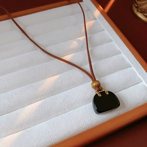 Close-up of black bag pendant necklace with brown wooden bead and leather cord