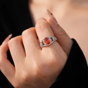 Detail of silver ring with orange oval zircon and pavé diamonds worn on a finger