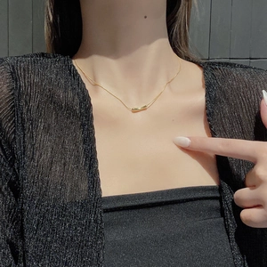Detail of a minimalist gold pea-shaped curved pendant necklace on a female collarbone
